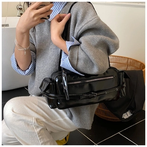 Detailed view of black patent leather underarm bag with silver hardware on model