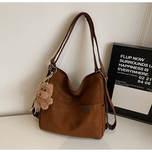 Detail view of caramel brown vintage tote bag with plush bear charm and side brand label