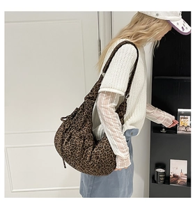Side view of leopard print dumpling bag with adjustable strap worn by model in room