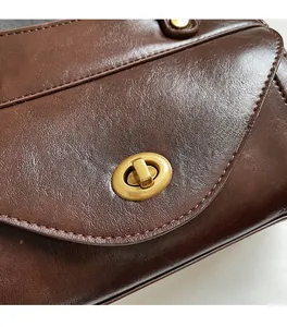 Close-up of brown faux leather bag featuring a gold oval twist lock and fine texture
