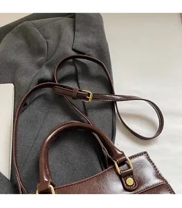 Detail of dark brown leather handbag with adjustable strap and golden metal rivets