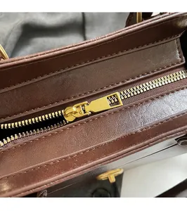 Detailed macro view of high-quality gold metal zipper and leather texture on a brown handbag