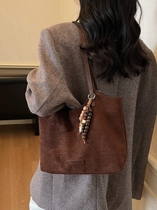 Sac cabas rétro en daim marron avec perles en bois, porté à l'épaule par un mannequin chic