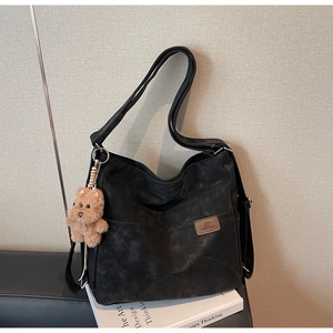 Detail view of vintage black tote bag with brown logo patch and plush bear accessory