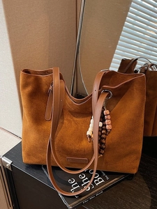 Grand sac cabas en daim marron foncé avec lanières en cuir et perles sous une douce lumière