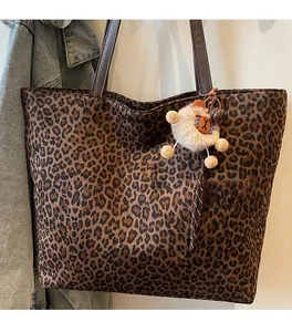 Detail of leopard print tote bag with brown leather handles and plush bear charm