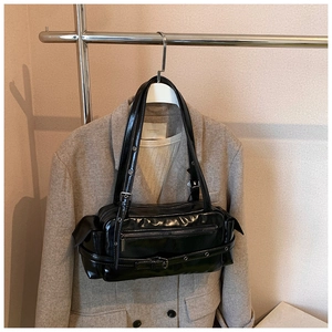 Detail of glossy black patent leather shoulder bag with vintage buckles and dual straps