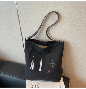 Detailed embroidery of church and leaves on a black canvas tote bag with leather straps