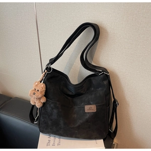 Detail of vintage matte suede tote bag with brown plush bear charm on a black sofa