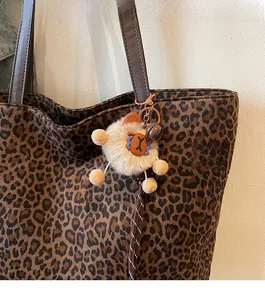 Close-up of a cute brown plush bear charm attached to a leopard print tote bag handle
