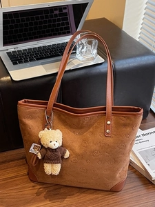 Brown suede tote bag with embossed bear patterns and plush bear keychain on wooden desk