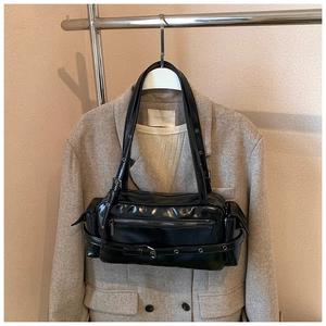 Detail of a black glossy underarm bag styled over a beige blazer on a clothing hanger
