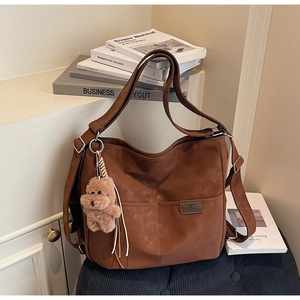 Detail of a brown tote bag with stitching, shoulder strap, and a cute teddy bear charm