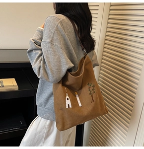 Detailed embroidery of church and trees on a brown canvas shoulder bag worn by model