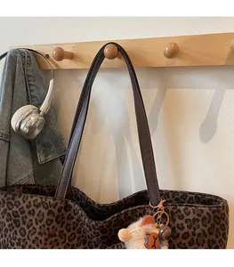 Detail view of leopard print tote bag with brown leather straps and lion plush charm