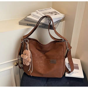 Detailed view of brown faux leather tote bag with plush puppy charm and front pocket
