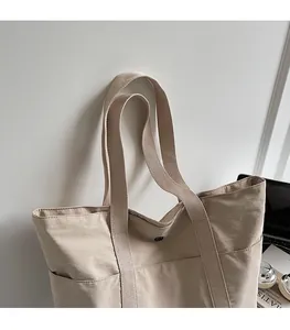 Detail of beige canvas tote bag showing wide shoulder strap and side pocket design