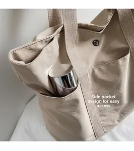 Detail of beige nylon tote bag side pocket holding a stainless steel water bottle