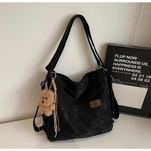 Close-up of black matte tote bag with leather logo patch and cute plush bear keychain