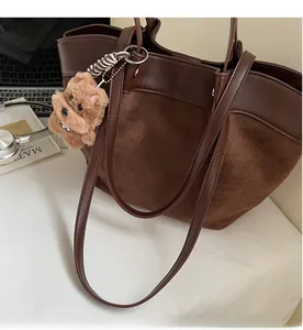Detail of large brown suede tote bag with plush bear charm and sturdy shoulder straps