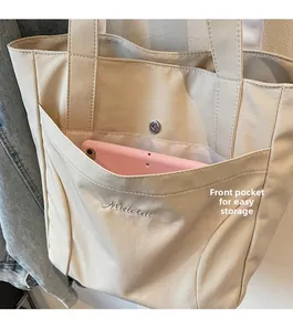 Close-up of beige canvas tote bag showing large front pocket holding a pink tablet