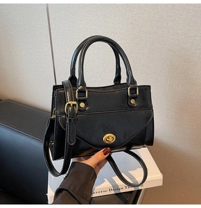 Close-up of the vintage black handbag featuring a polished gold ring twist lock and handle