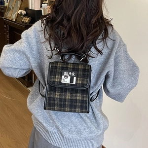 Détail d'un sac à dos vintage à carreaux avec broderie ours sur pull gris