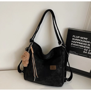 Detail of black matte tote bag with brown leather label and plush bear keychain accessory