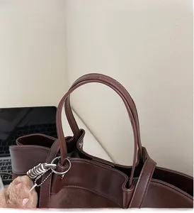 Detail of sturdy leather handle on dark brown tote bag with cute plush bear charm