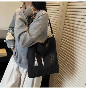 Detail of vintage embroidery pattern on a black canvas tote bag worn by a model