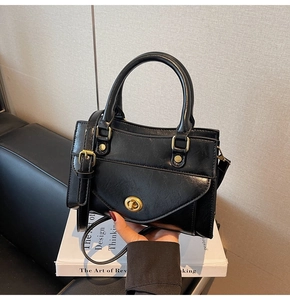 Detail of black faux leather handbag with golden twist-lock and top handle