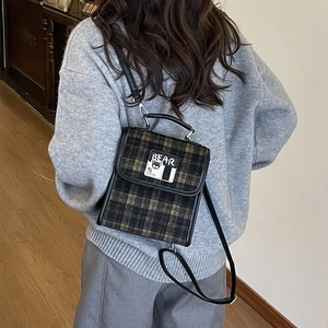 Détail du sac à dos à carreaux vintage avec patch d'ours et finitions en cuir noir