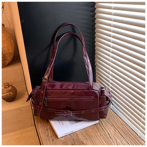 Close-up of retro deep burgundy shoulder bag with metallic eyelet straps and glossy finish