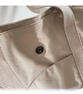 Close-up of beige nylon tote bag showing black metal logo and textured woven handle