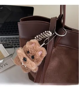 Detail of a brown plush bear charm attached to a suede tote bag with metal chain