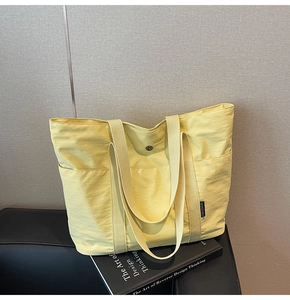 Close-up of light yellow tote bag featuring dual front pockets and magnetic buckle closure