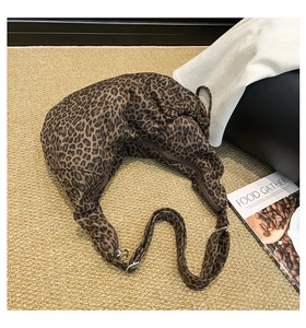 Detail of leopard print crescent bag with adjustable strap and zipper on textured rug