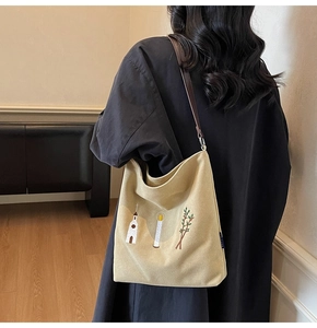 Detailed view of embroidery pattern on beige canvas shoulder bag shown with the model