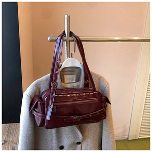 Close-up of a burgundy glossy shoulder bag with metal eyelets and adjustable buckle straps