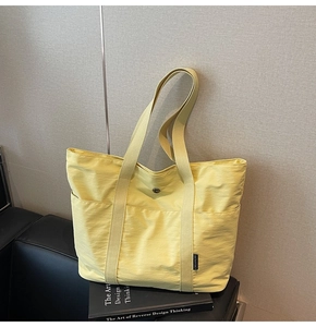 Close-up of yellow canvas tote bag with side pockets and black label on book background