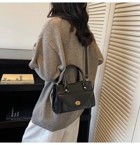 Close-up of black glossy leather handbag with gold oval twist lock and sleek crossbody strap