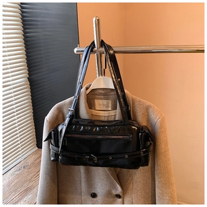 Detail of a black glossy leather shoulder bag with metallic zippers and decorative belts