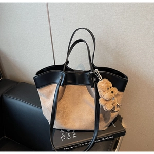 Macro detail of khaki suede and black leather patchwork tote with a plush bear charm