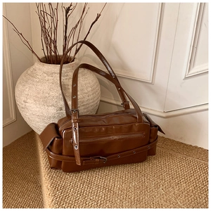 Detail of brown glossy PU leather Boston bag with decorative buckle and metal eyelet strap