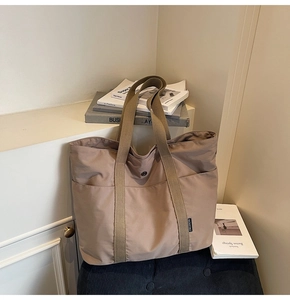 Detail of khaki nylon tote bag showing wide straps and functional front pockets