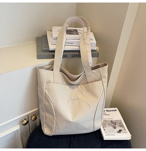 Detail of cream canvas tote bag featuring white Midolai embroidery and a front pocket