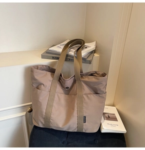 Detail of warm beige nylon tote bag featuring durable woven straps and side logo label