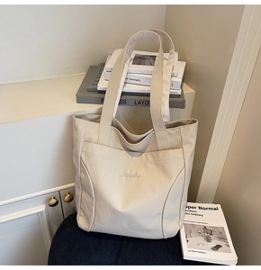 Detailed view of cream canvas tote bag featuring Midolal embroidery and front pocket
