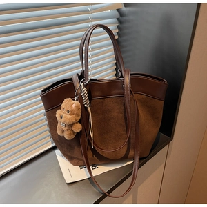 Detailed view of large brown tote bag with suede texture and cute teddy bear charm
