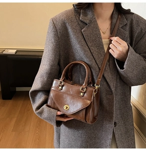 Detailed view of dark brown vintage handbag with gold clasp and dual handles on a model